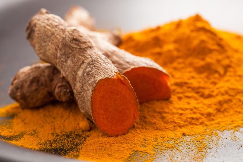 a closeup image of a pile of turmeric powder with a fresh turmeric rhizomes on it