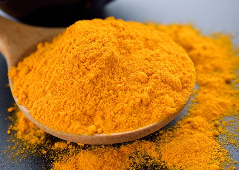 closeup image of a wooden spoon with turmeric powder with some of it spilling on the black-colored surface