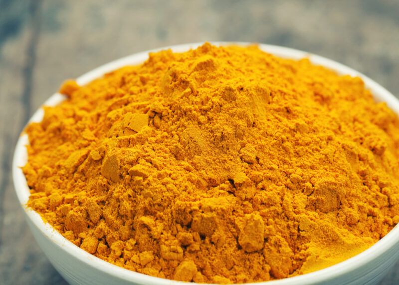 on a wooden surface is a closeup image of a white bowl full of turmeric powder