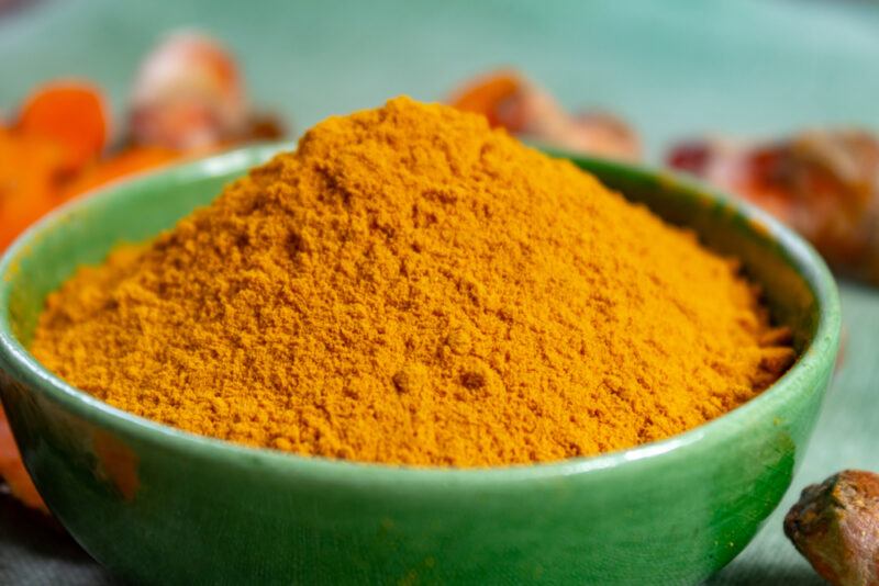 a closeup image of a green bowl with turmeric powder, with fresh turmeric rhizomes around it