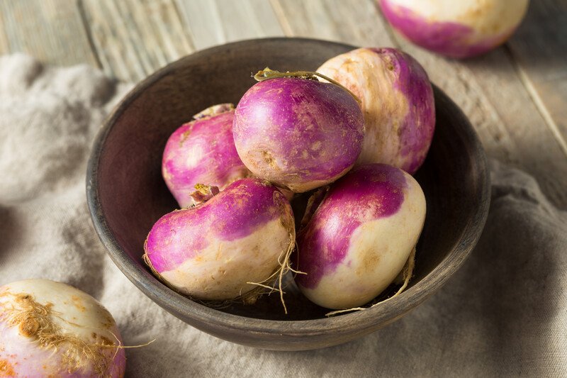 a closeup image of a wooden bowl full of turnips, resting on a wooden table