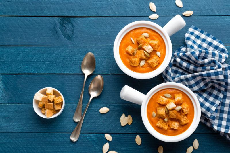 two bowls of pumpkin soup topped with croutons, on a blue table