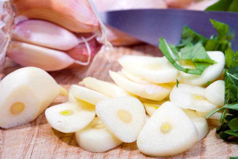 slivers of garlic beside a whole unpeeled bulb of garlic