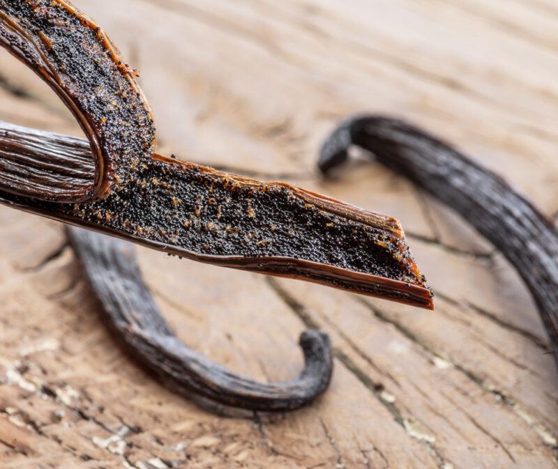 on a rustic looking wooden surface is a couple of vanilla pods, with one partially split open