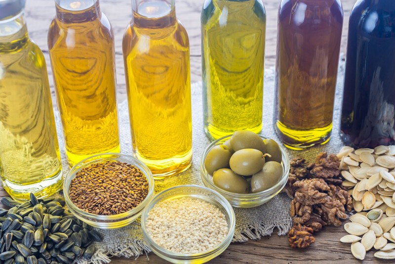 different jars full of vegetable oils with little bowls full of olives, walnuts, sunflower seeds, sesame seeds, flaxseeds, and pumpkin seeds