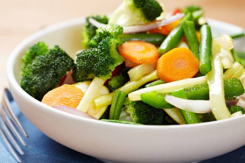 a closeup image of a white shallow bowl with sauteed vegetables including broccoli, carrots, beans, and others 