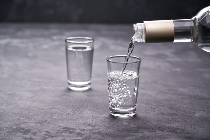 on a black surface with a couple of shot glasses, one with vodka and one with vodka being poured into it