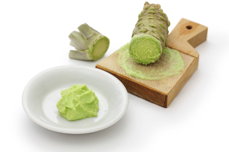 fresh wasabi on a wooden grater and a white saucer with freshly grated wasabi on it 