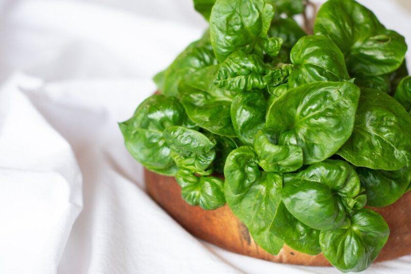 on a crumpled white cloth is a wooden dish full of watercress