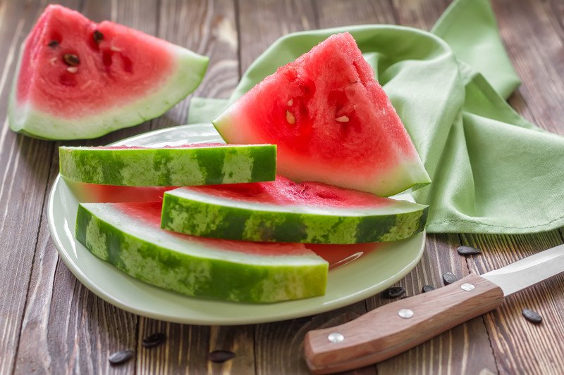 closeup image of a plate of cut watermelon with knife on its side and green table napkin and one piece of cut watermelon at the back