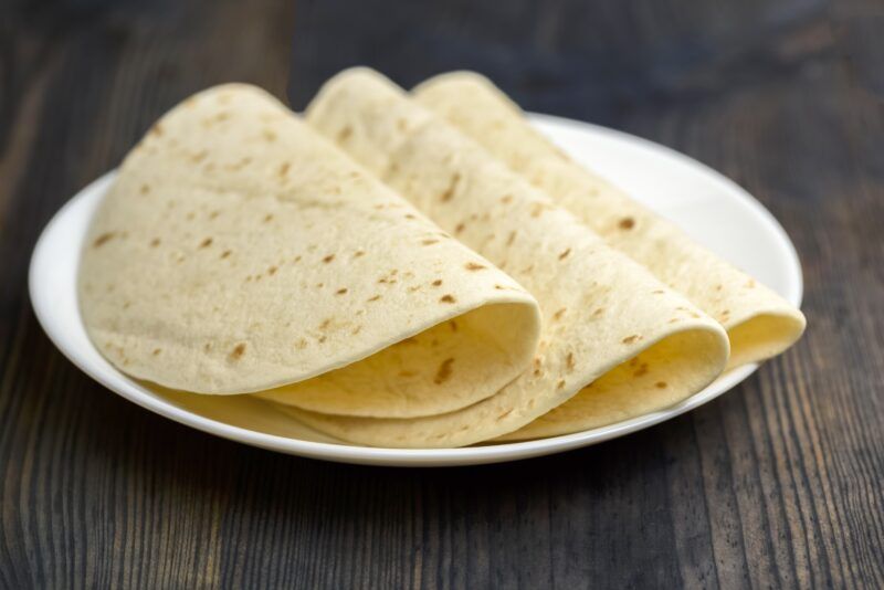 on a dark wooden surface is a white plate with wheat tortillas