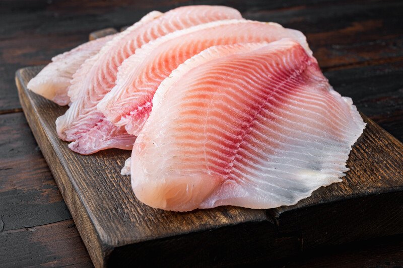 closeup image of a white fish fillet on a dark wooden chopping board