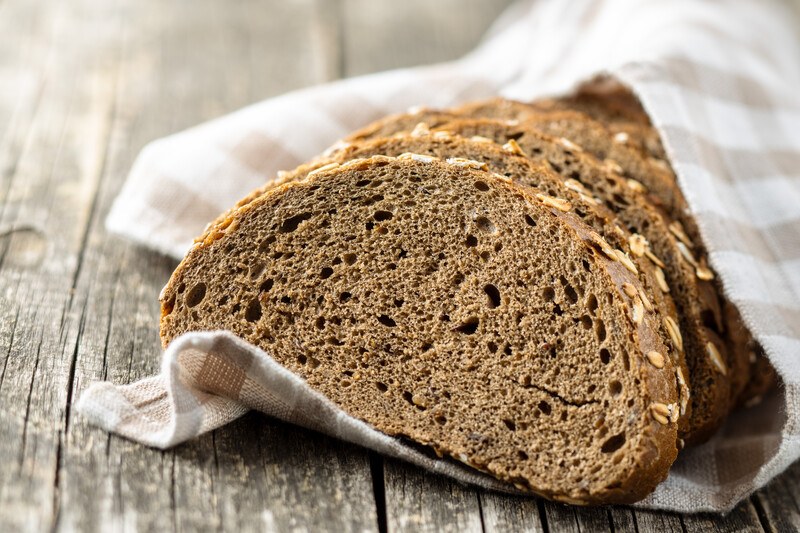 closeup image of sliced whole grain bread wrapped with stripped white and brown table napkin