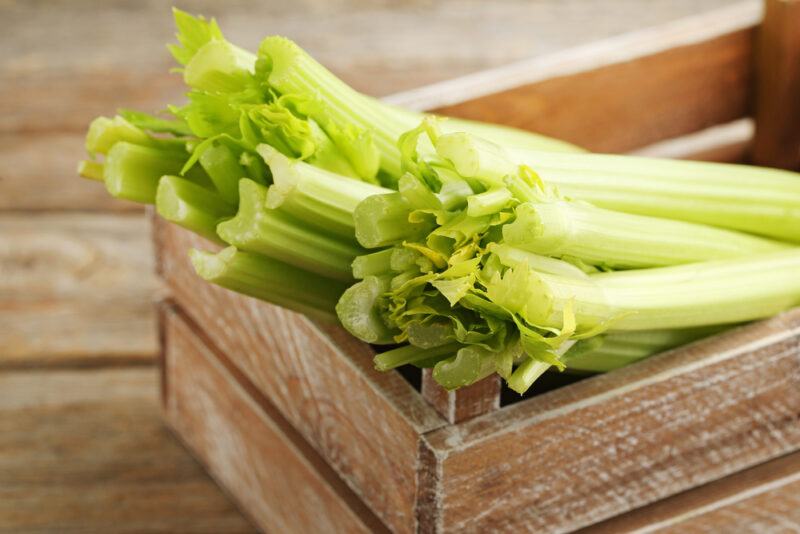 on a wooden surface is a wooden crate full of celery stalks