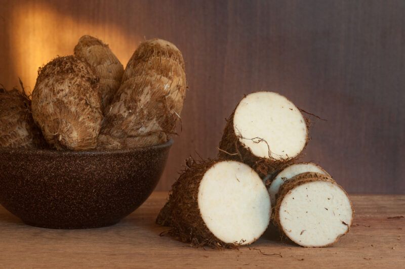 on a wooden surface are cut yams with a brown bowl beside it with whole yams