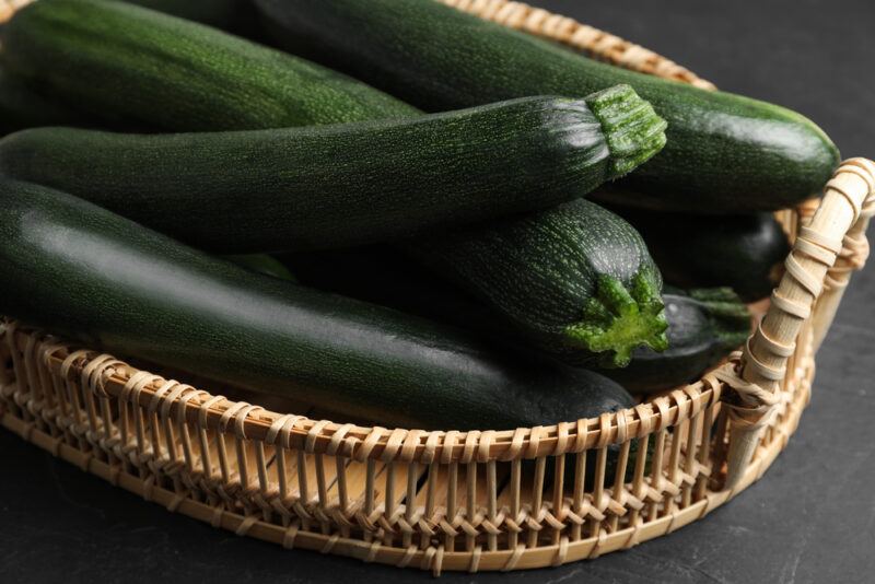 closeup image of a basket of whole zucchinis on a dark surface